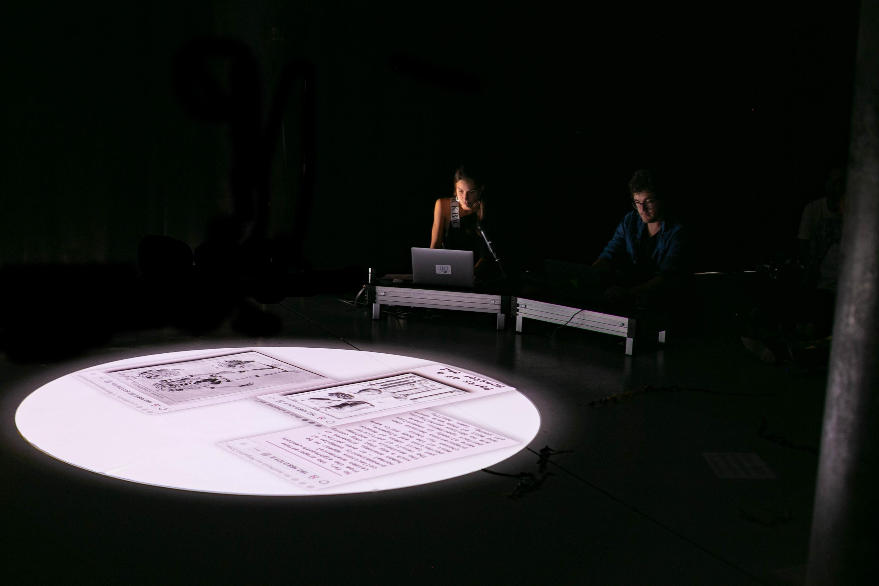 image of the two performers in their computers and performance set up with a circular projection of the floor